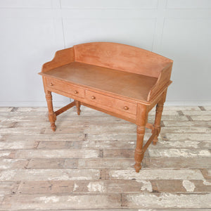 A large vintage pine washstand with a shaped gallery back and two drawers, each fitted with wooden knobs. Raised on four turned legs, this rustic farmhouse piece can be used as a washstand in a bathroom or as a dressing table in a bedroom.