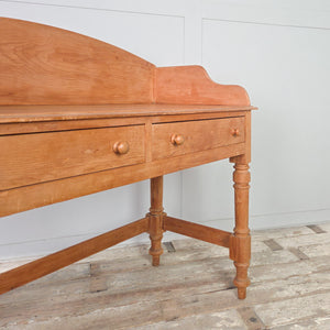 A farmhouse-style vintage pine console table with two drawers and a shaped gallery back, raised on four turned legs. This characterful piece is well suited to use as a hall table in a hallway or as a side table within a living space.