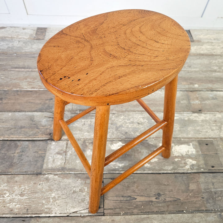 Decorative mid-century stool with oval seat and supportive legs in elm.
