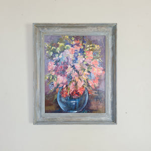 A framed vintage oil painting depicting an abundant bouquet of mixed flowers in a blue ceramic vase, painted in warm pinks and reds.
