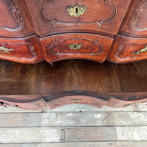 French serpentine walnut chest of drawers or commode from the 19th century, with decorative brass handles and escutcheons and a shaped apron at the base.
