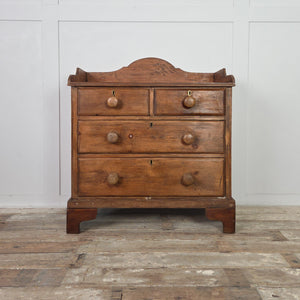 A Victorian rustic pine four-drawer chest with two short drawers over two long, wooden knobs and a shaped gallery along the back. Finished in a darker stain, this farmhouse style storage chest provides versatile cottage style bedroom drawers.