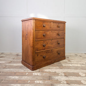 A Victorian pine storage chest with five drawers arranged two over three, original decorative knobs and a rich rustic patina. The plinth base and waxed finish add a cottage style feel to this practical farmhouse style piece.