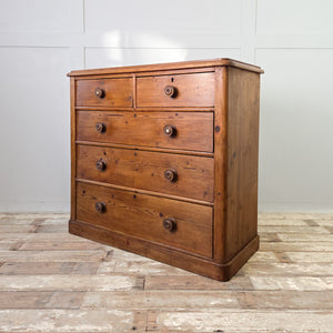 A Victorian rustic pine chest of drawers with five roomy drawers, original wooden knobs including mother-of-pearl inlays, and a simple plinth base. The waxed finish enhances its country house style presence as dependable bedroom drawers.