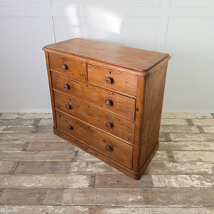 A country house style Victorian pine chest with five drawers, wooden knobs and subtle mother-of-pearl details. The waxed patina and plinth base contribute to its rustic pine character as a solid storage chest.