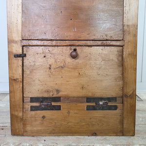 This early 20th century antique workshop drawer unit is built from mixed timber and includes two drawers and a lower cupboard with a drop-down front and large metal hinges. Its rugged industrial character makes it a practical option for use as a bedside table in the bedroom or an end table in the hallway or living room.