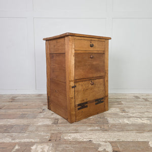 An early 20th century antique workshop drawer unit constructed from mixed timbers, with two drawers above a lower cupboard accessed by a drop-down door with large metal hinges. The industrial nature of the piece makes it a practical choice for use as a bedside table in the bedroom or an end table in the hallway or living room.