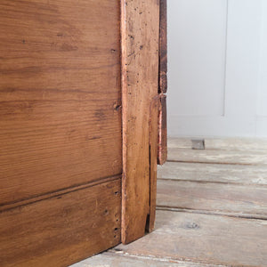 This early 20th century antique workshop drawer unit features two drawers and a lower cupboard concealed behind a drop-down front. Constructed from mixed timbers with large metal hinges and sealed in rustic pine wax, it suits use as a bedside table in the bedroom or an end table in the hallway or living room.
