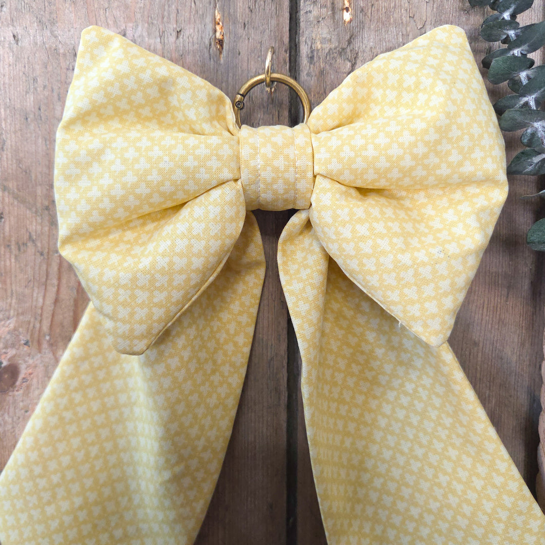 A handmade decorative Country House Bow in vintage yellow patterned fabric with padded body and elongated tails. Finished with brass hanging ring, this bow is perfect for rustic interiors, wedding décor, or gifting.
