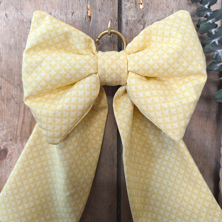 A handmade decorative Country House Bow in vintage yellow patterned fabric with padded body and elongated tails. Finished with brass hanging ring, this bow is perfect for rustic interiors, wedding décor, or gifting.