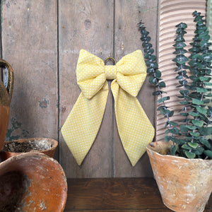 Handmade Country House Bow from Jennings & Cox, created in vintage yellow patterned fabric with structured padded design. Each bow is made in limited numbers with tapering tails and finished with an antiqued brass ring for hanging.