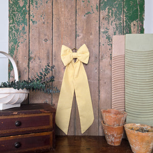 A large handmade bow from Jennings & Cox, created in vintage yellow patterned fabric. This Country House Bow is padded and structured with long tails and finished with an antiqued brass hanging ring, designed for versatile styling.
