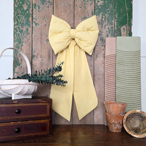 Handmade vintage fabric bow in sunny yellow patterned fabric, padded and structured with tapering tails. This Jennings & Cox Country House Bow is made in limited numbers and finished with a brass hanging ring for home or event décor.