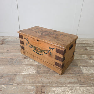 French folk art chest in pine with hand-painted garland of flowers tied with blue ribbon bows at each corner
