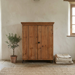 Vintage pine cupboard from the early 20th century with two vertical planked doors, an overhanging cornice, and bracket style feet with cut out detailing.
