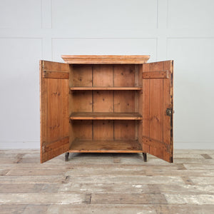 Rustic pine storage cupboard with two vertical planked doors and fixed internal shelving, finished with an overhanging cornice and bracket style feet.