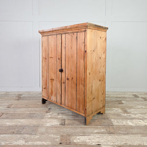 Early 20th century pine cupboard cabinet with two vertical planked doors, overhanging cornice, and cut out detailing to the sides above bracket feet.