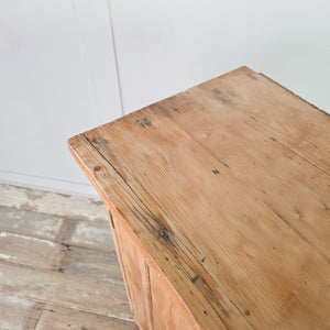 Antique farmhouse pine cupboard with two vertical planked doors, an overhanging cornice, and bracket style feet with cut out detailing to the sides.

