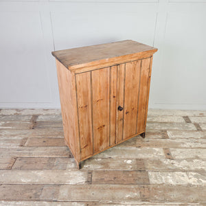 Early 20th century rustic pine cupboard with two doors, dark round knob likely bakelite, and bracket style feet with cut out detailing to the sides.

