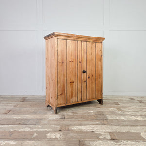 Two door pine cupboard from the early 20th century with vertical boarded doors, a dark round plastic knob likely bakelite, and bracket style feet.