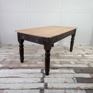 Antique Victorian farmhouse dining table with a planked sycamore top and dark painted pine base, featuring chunky turned legs and a single drawer with glass knobs.