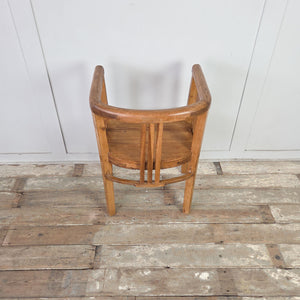 Two early 20th century pine tub chairs with barrel-back silhouette, wrap-around curved rail forming arms and back, slatted side and back supports, and deep seats on square legs.